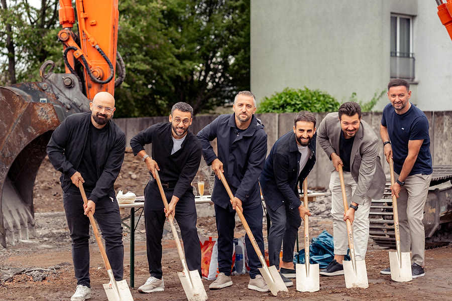 Spatenstich SCUOLA in Killwangen: sechs Personen mit Schaufeln vor dem Bagger, August 2026